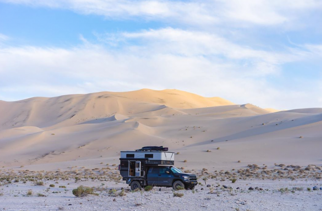 Toyota Tundra Camper in the middle of a sandy desert with cloudy blue skies above.