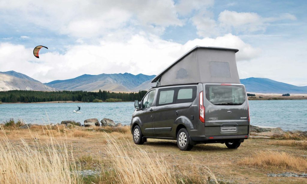 Ford Transit Nugget by a lake with the pop topped, and a kite-surfer in the background