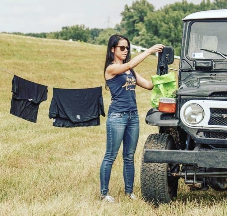 Woman hanging up washing from scrubba wash bag next to a Land Rover.