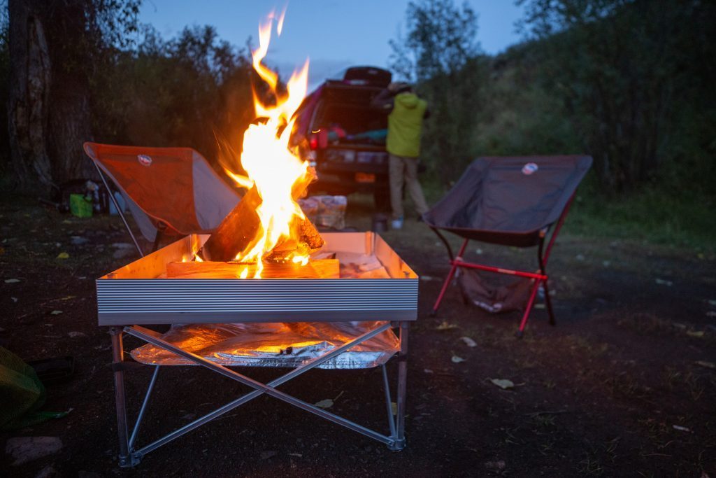 The pop up pit in action on grass near a camper and two chairs