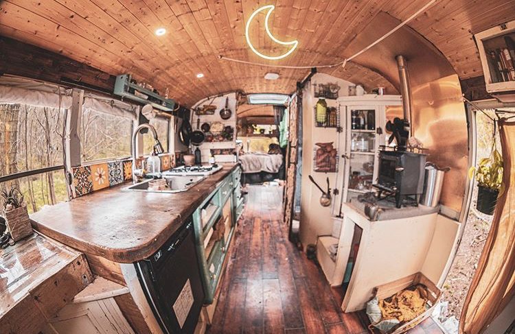 Wooden bus interior with kitchen, wood burner and bedroom in the back.