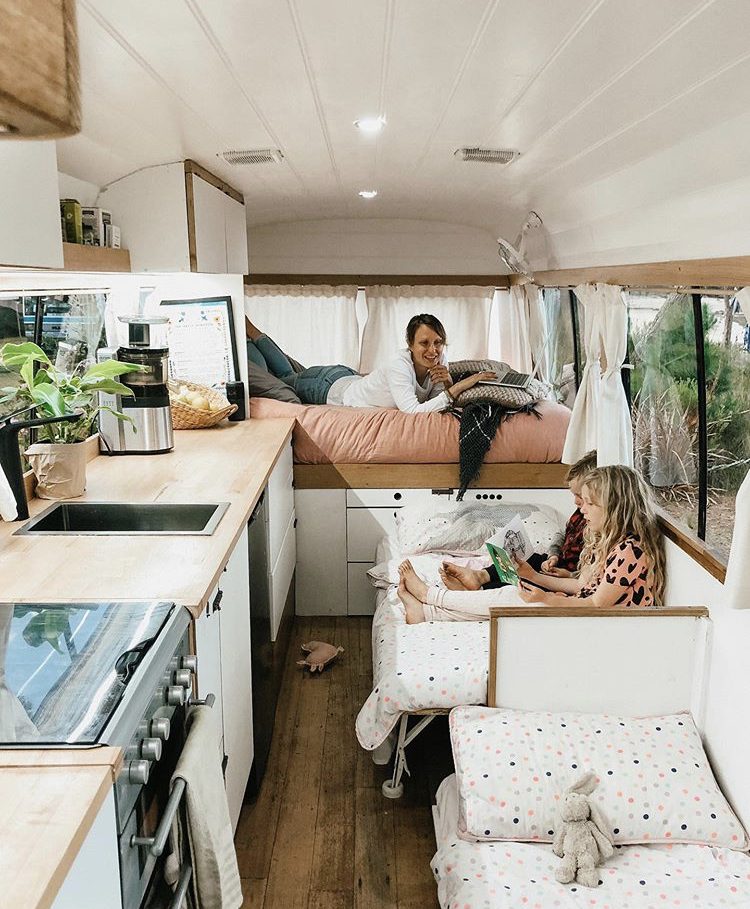 Custom van ideas- woman lying on bed with two kids reading books on their single beds opposite kitchen.