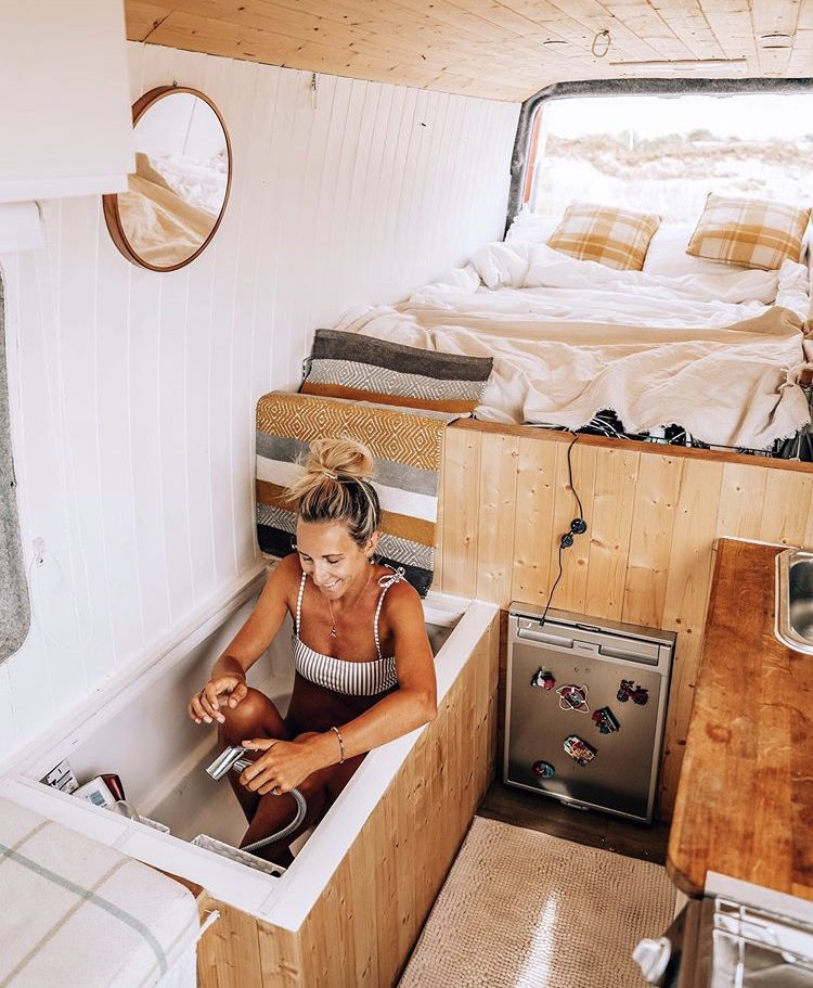 Woman sat in bathtub inside her van at the foot of static double bed.