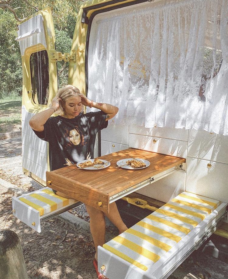Back of van with pull out wooden table and yellow and white stripy pull out seats with woman sat on one.