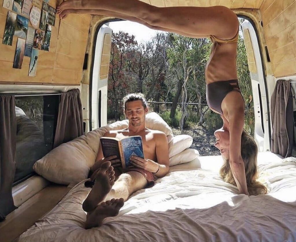 Woman doing yoga and man reading on bed in campervan