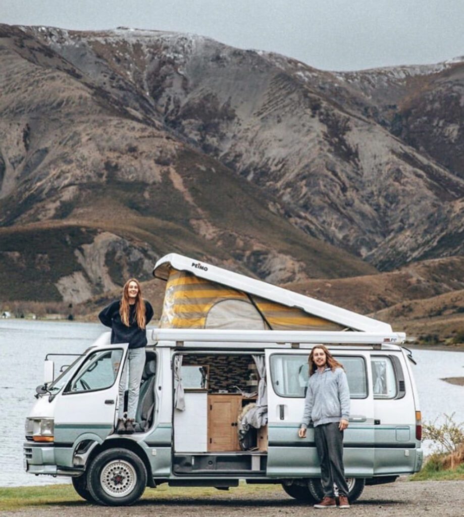 Pop top camper with roof up infront of lake and mountains