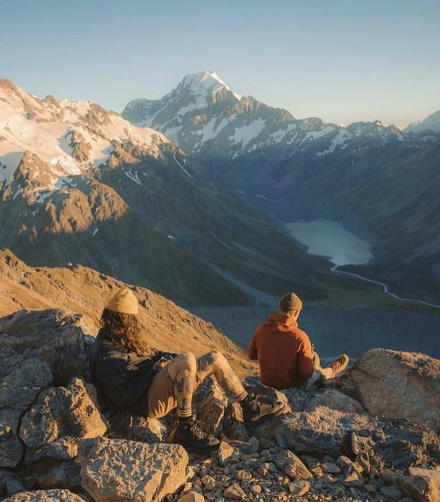 Two men sat in shorts and hats on mountain