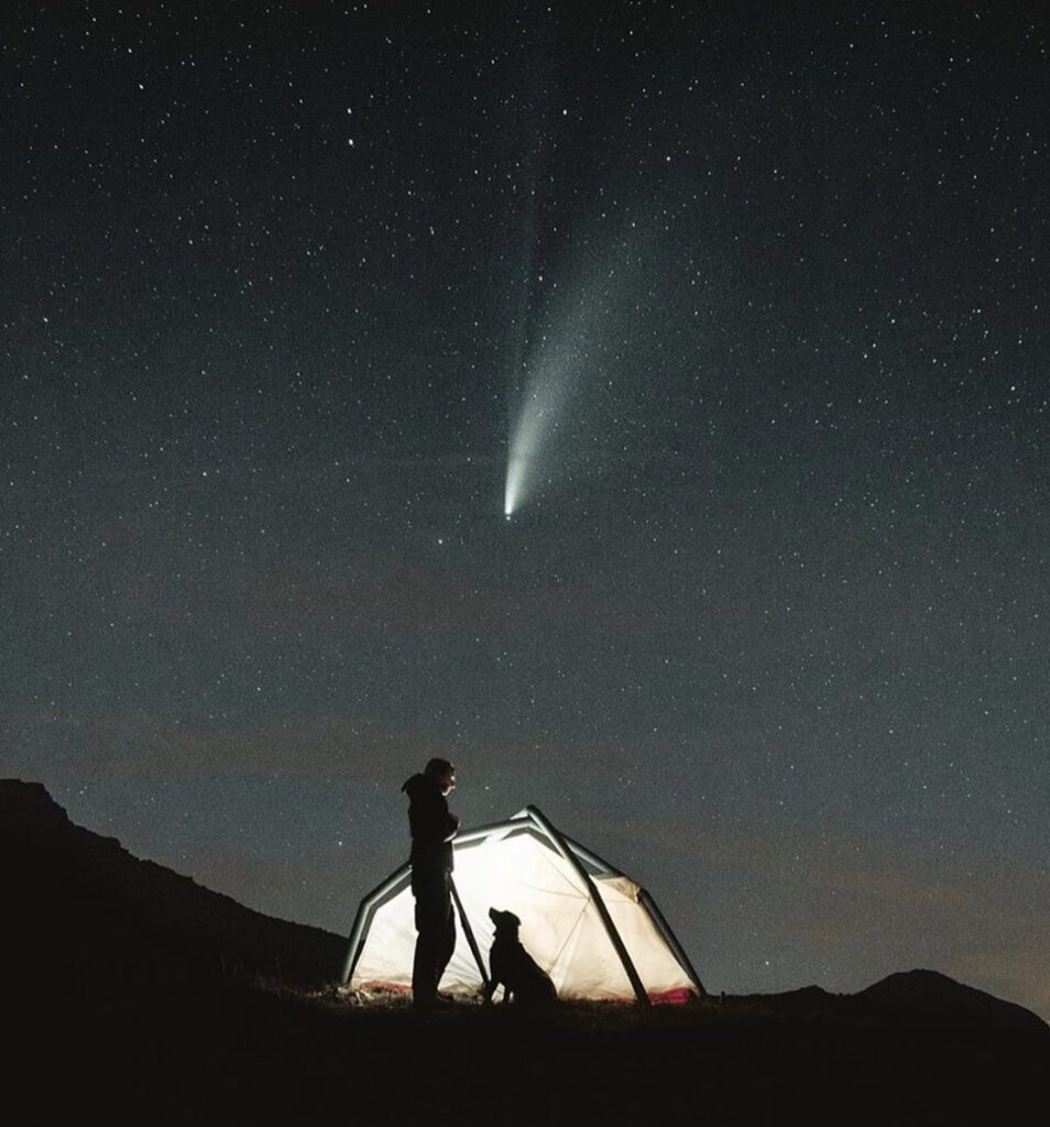 Sillouette of man and dog against lit up tent under the stars