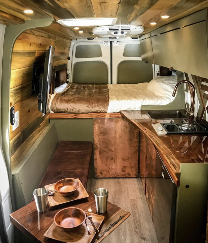 Dark green van with bed at backa nd kitchen and seating in front