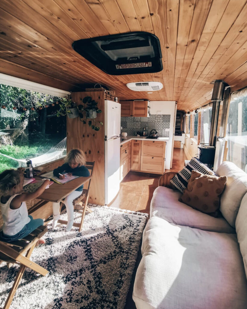 Bus interior with kids say inside at desk opposite the sofa and infront of kitchen