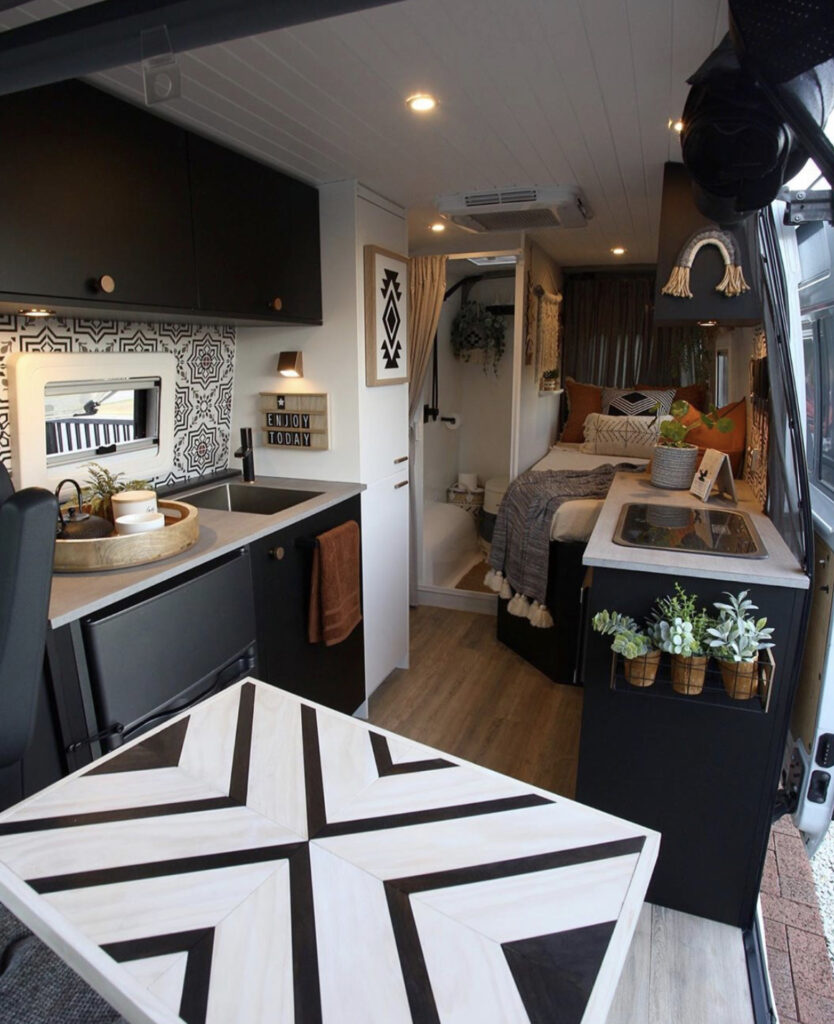 Conversion Vans - Single bed and bathrrom at the beach, kitchen and table at fron in moody colours